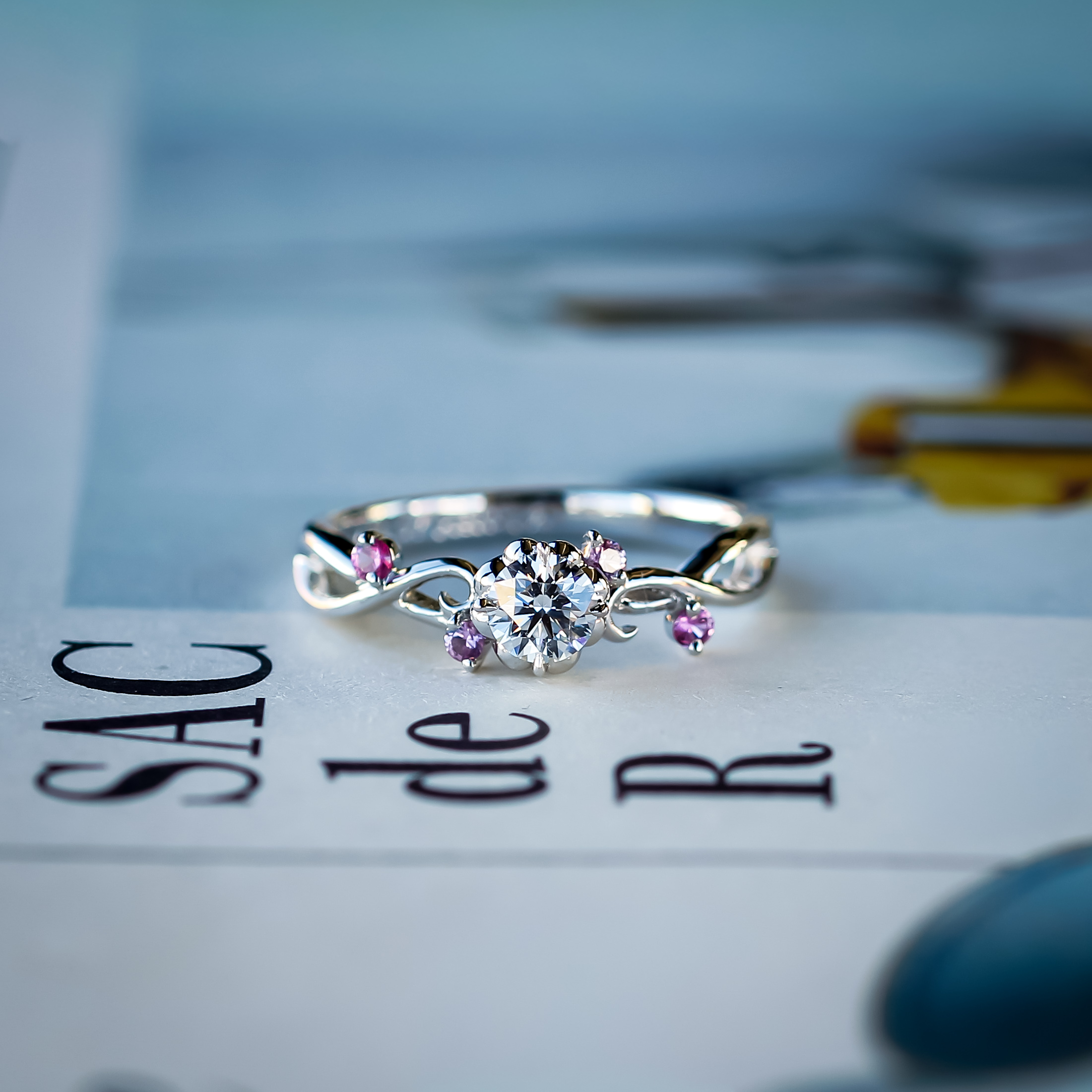 メレダイヤモンドをピンクサファイアにアレンジして、センターダイヤモンドが花シャトンで作られたお花をおモチーフにした婚約指輪